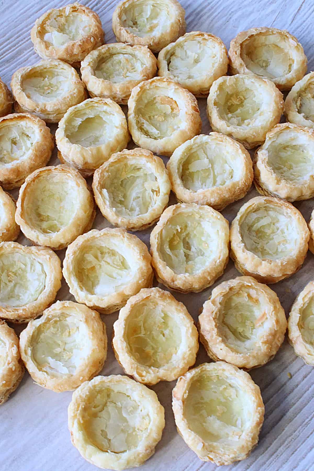 Flakey puff pastry appetizer cups on a plate waiting to be filled.