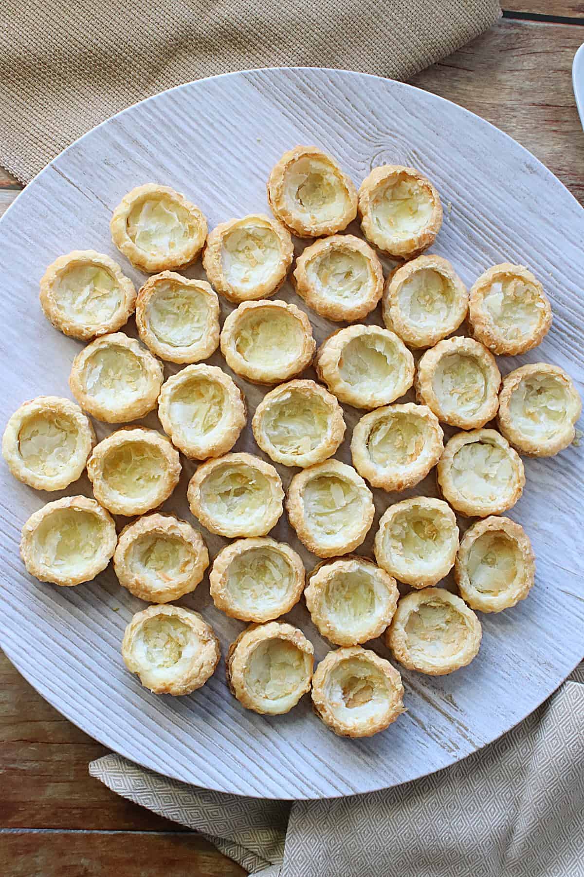 A round platter filled with baked round Puff Pastry Appetizer Cups waiting to be filled.