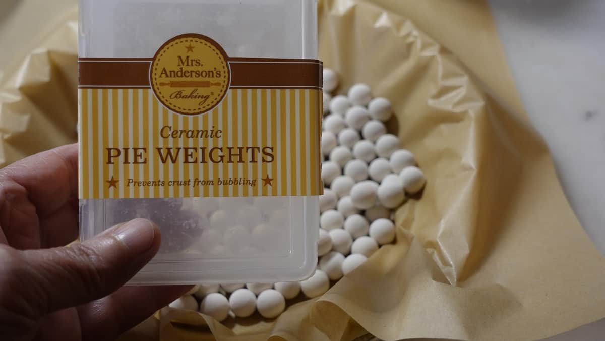 A hand holding an empty box of pie weights above an unbaked pie.