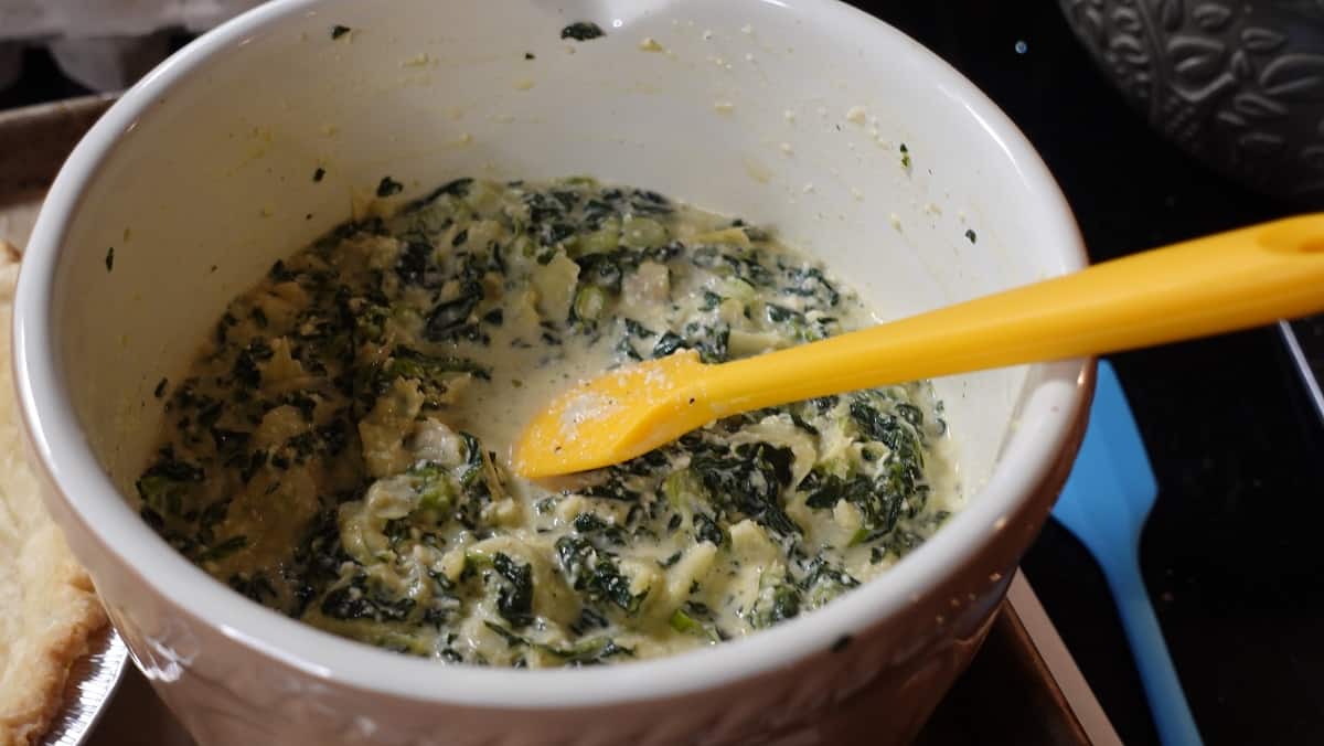 A mixture of eggs, spinach and chopped artichokes in a bowl.