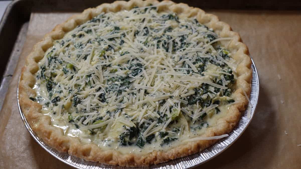 A unbaked Spinach and Artichoke Quiche getting ready to go into the oven.