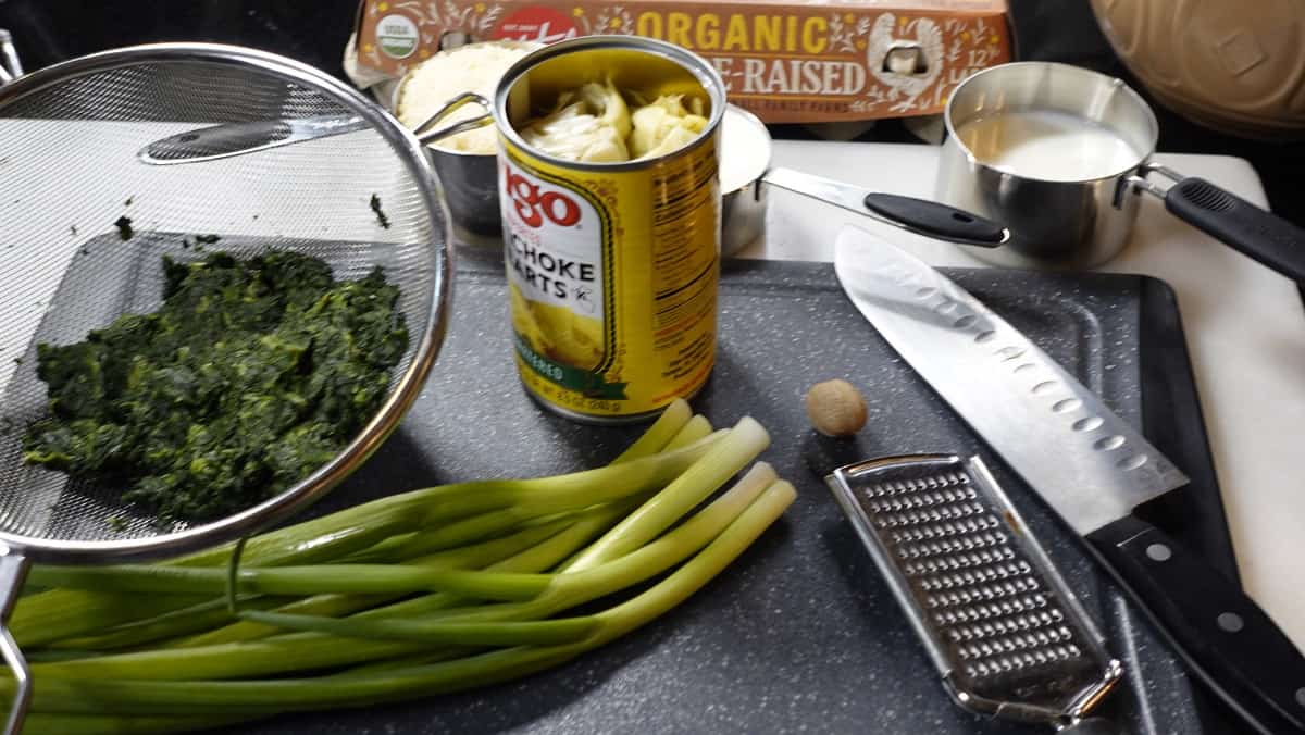 Ingredients on a cutting board for making a spinach and artichoke quiche.