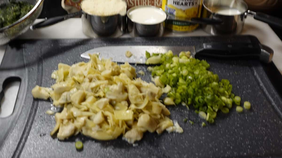 Chopped artichokes and scallions on a cutting board for making spinach and artichoke quiche.