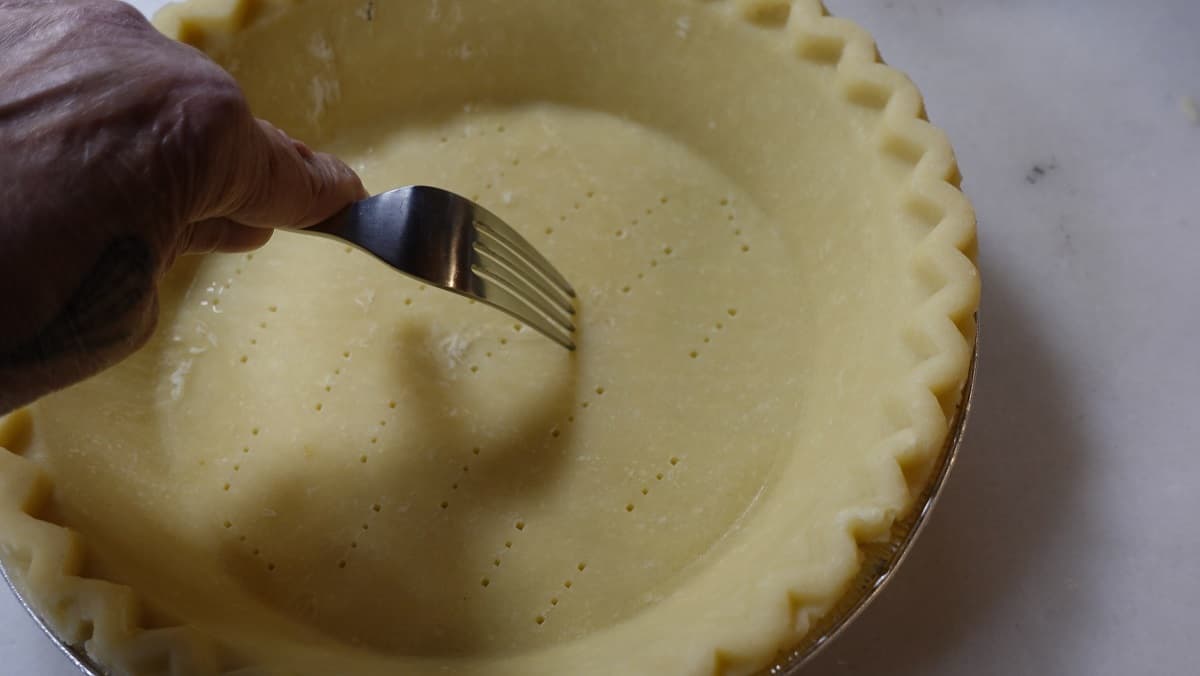 A fork docking an unbaked pie crust.