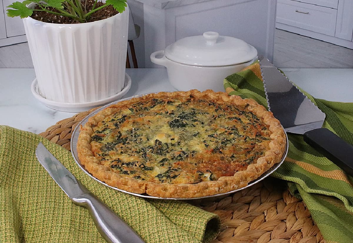 Green napkins along with a knife around a quiche.