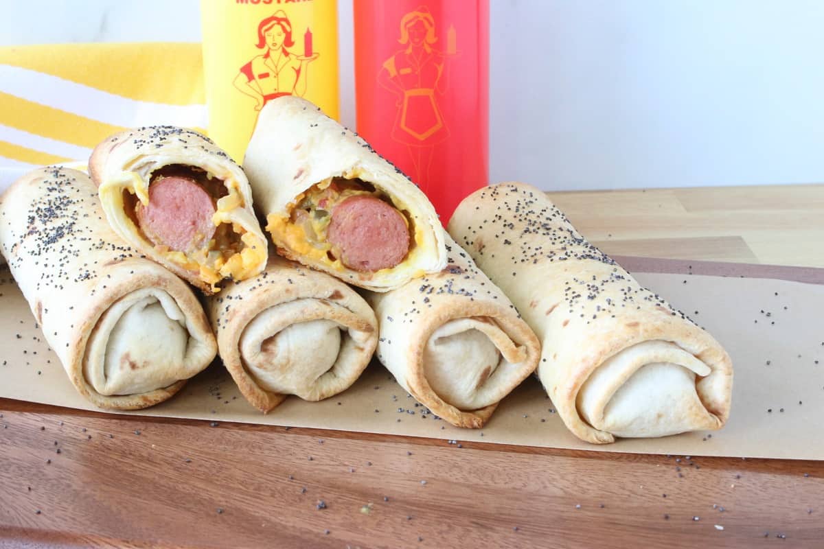 A stack of Burrito Dogs on a wooden platter with the one on top cut in half.