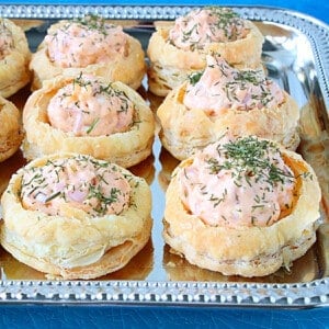 Pretty Ham and Cheese Puff Pastry Appetizer Cups topped with dill on a pretty silver platter.