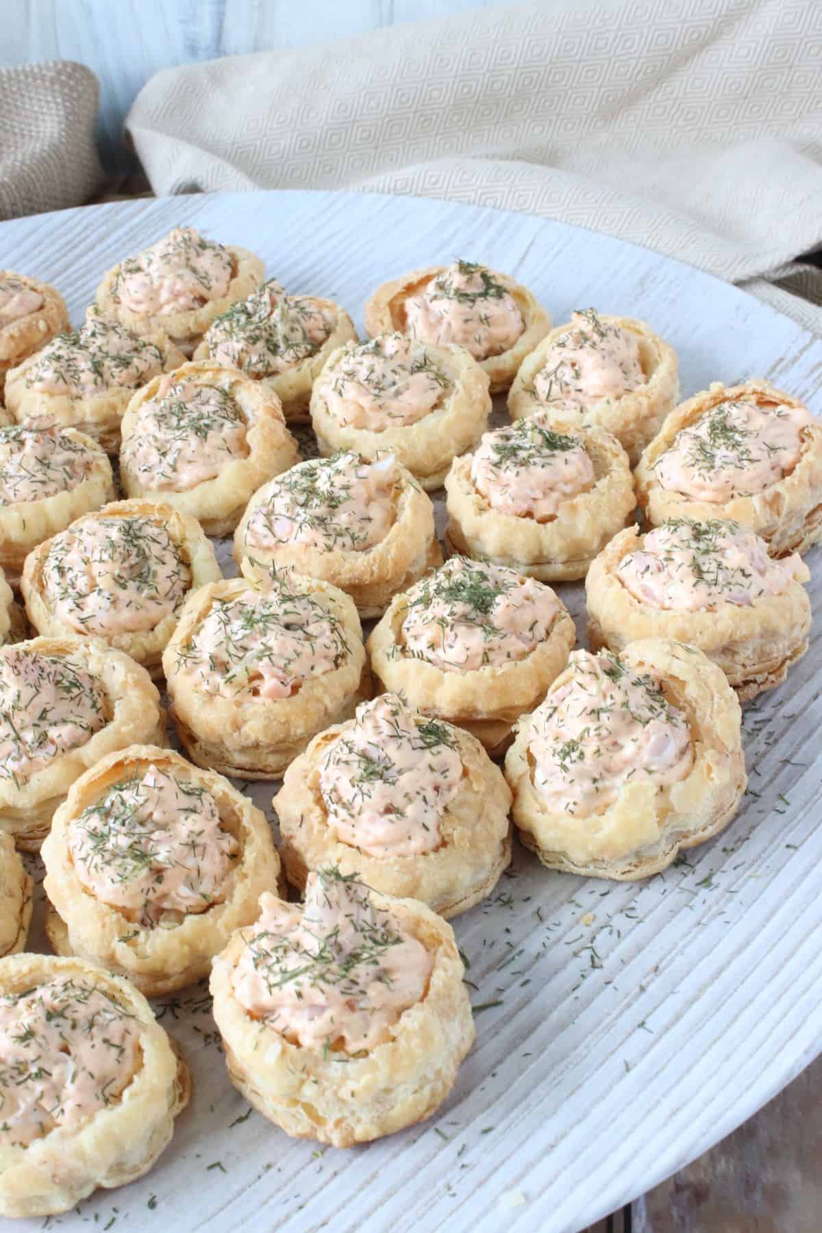 A causal round platter filled with Ham and Cheese Puff Pastry Appetizer Cups and garnished with dill.