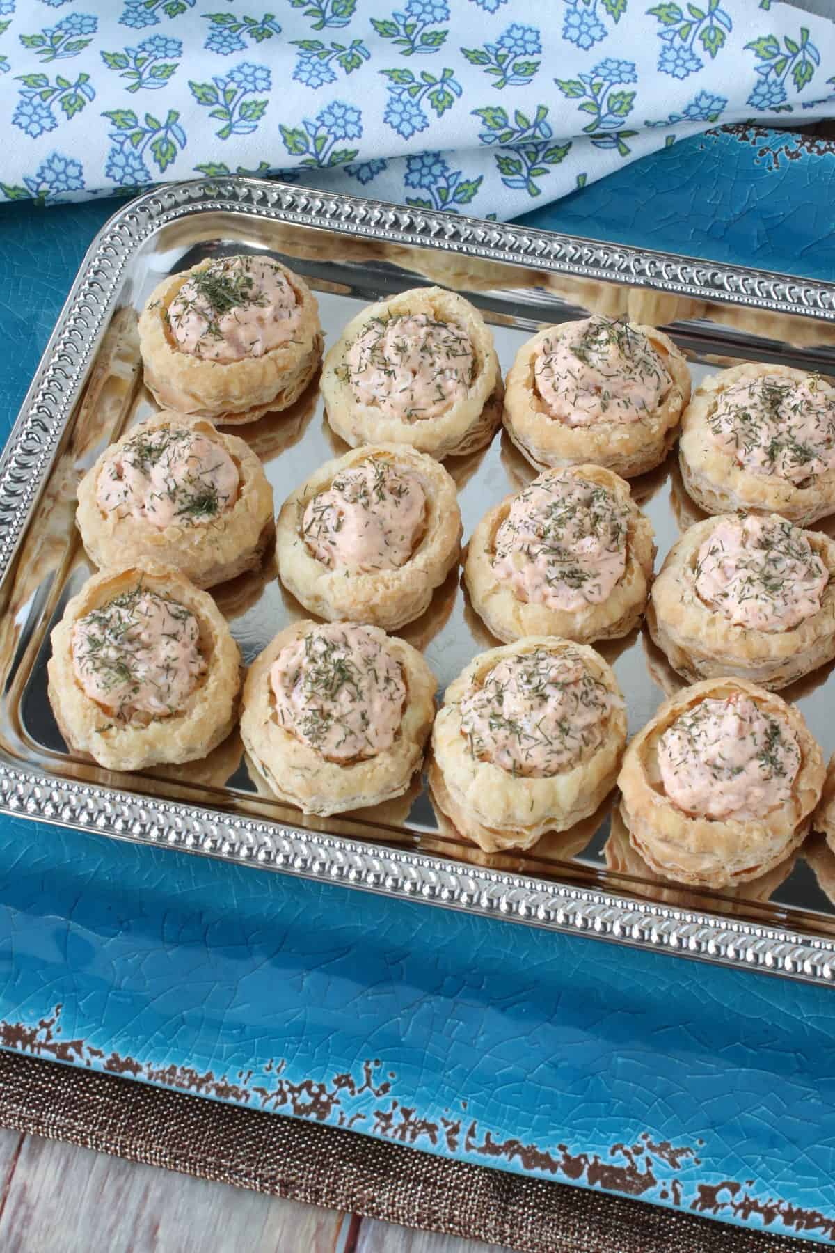 A silver tray filled with ham and cheese puff pastry appetizer cups along with a blue and green floral napkin.