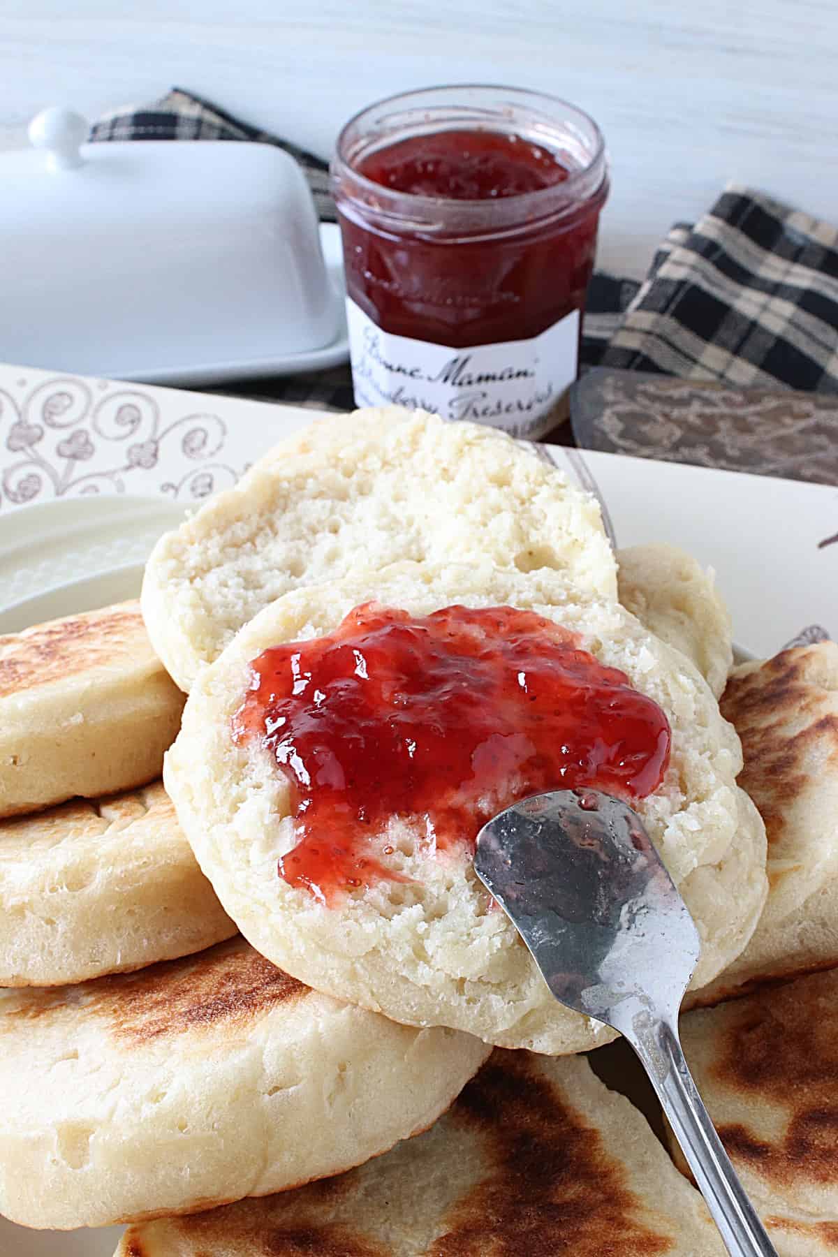 A jam spoon smearing strawberry jam on a Homemade English Crumpet.
