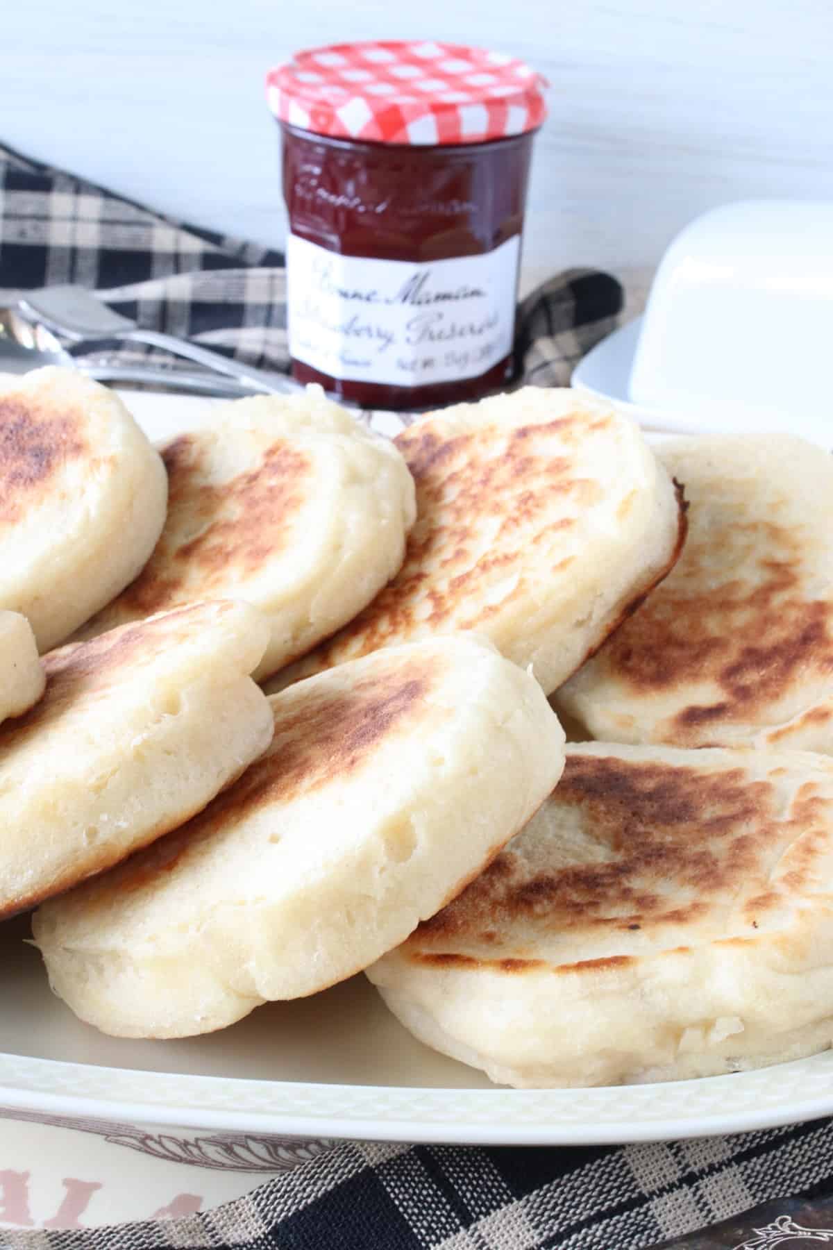 A platter filled with Homemade English Crumpets along with a jar of strawberry jam in the background.