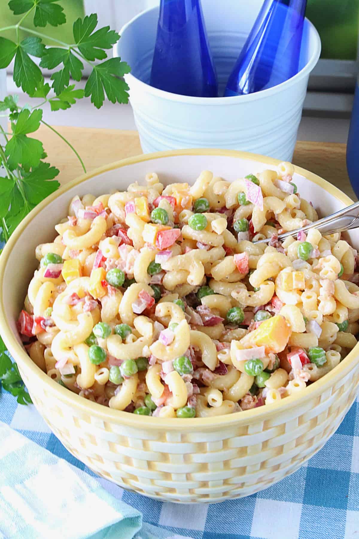 A serving bowl filled with Chilled Macaroni and Pea Salad on a blue and white checked tablecloth.