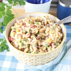 A bowl filled with Macaroni and Pea Salad along with a serving spoon.