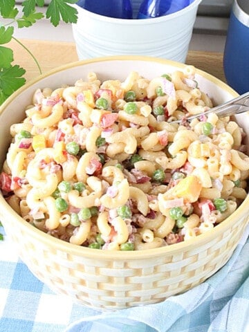 A bowl filled with Macaroni and Pea Salad along with a serving spoon.
