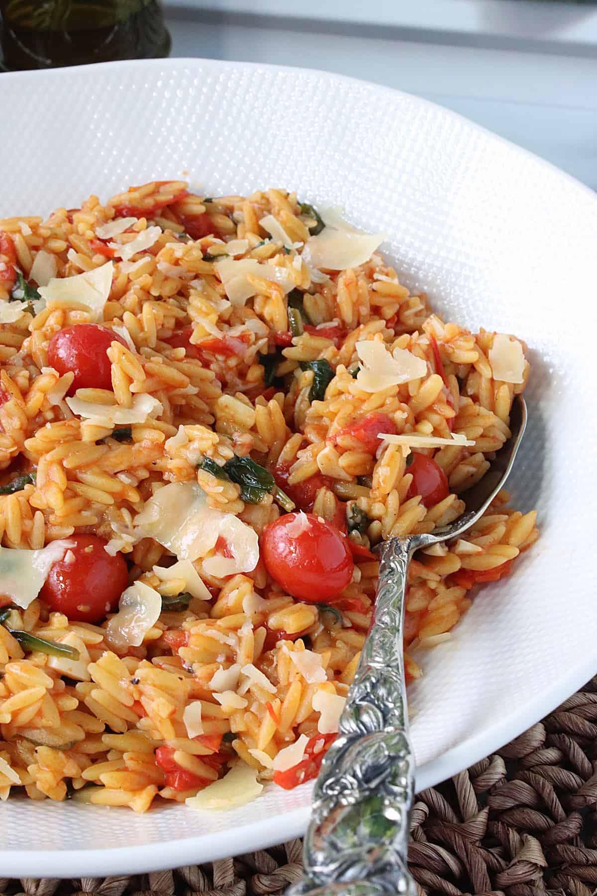 A serving spoon in a large bowl of Orzo Pasta with Spinach and Tomatoes.