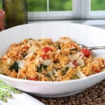 A white bowl filled with One Pan Orzo with Tomatoes and Spinach with a serving spoon.