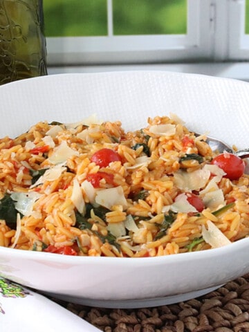 A white bowl filled with One Pan Orzo with Tomatoes and Spinach with a serving spoon.