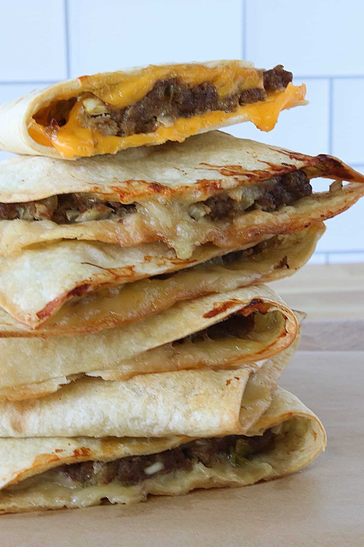 A stack of cut Burgerdillas with cheese on a wooden cutting board. 