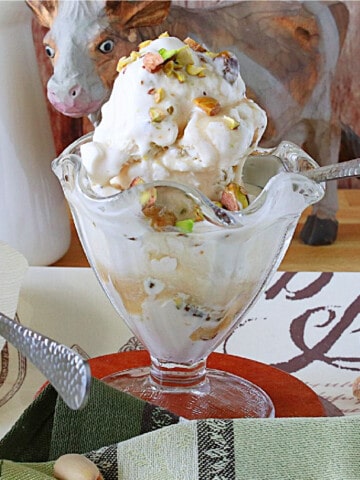 A glass parfait dish filled with Maple Pistachio Ice Cream with chopped pistachios on top.