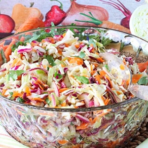 A glass bowl filled with No Mayo Sweet Sour Coleslaw along with a serving spoon.