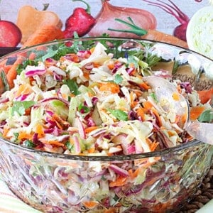 A glass bowl filled with No Mayo Sweet Sour Coleslaw along with a serving spoon.