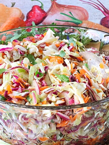 A glass bowl filled with No Mayo Sweet Sour Coleslaw along with a serving spoon.