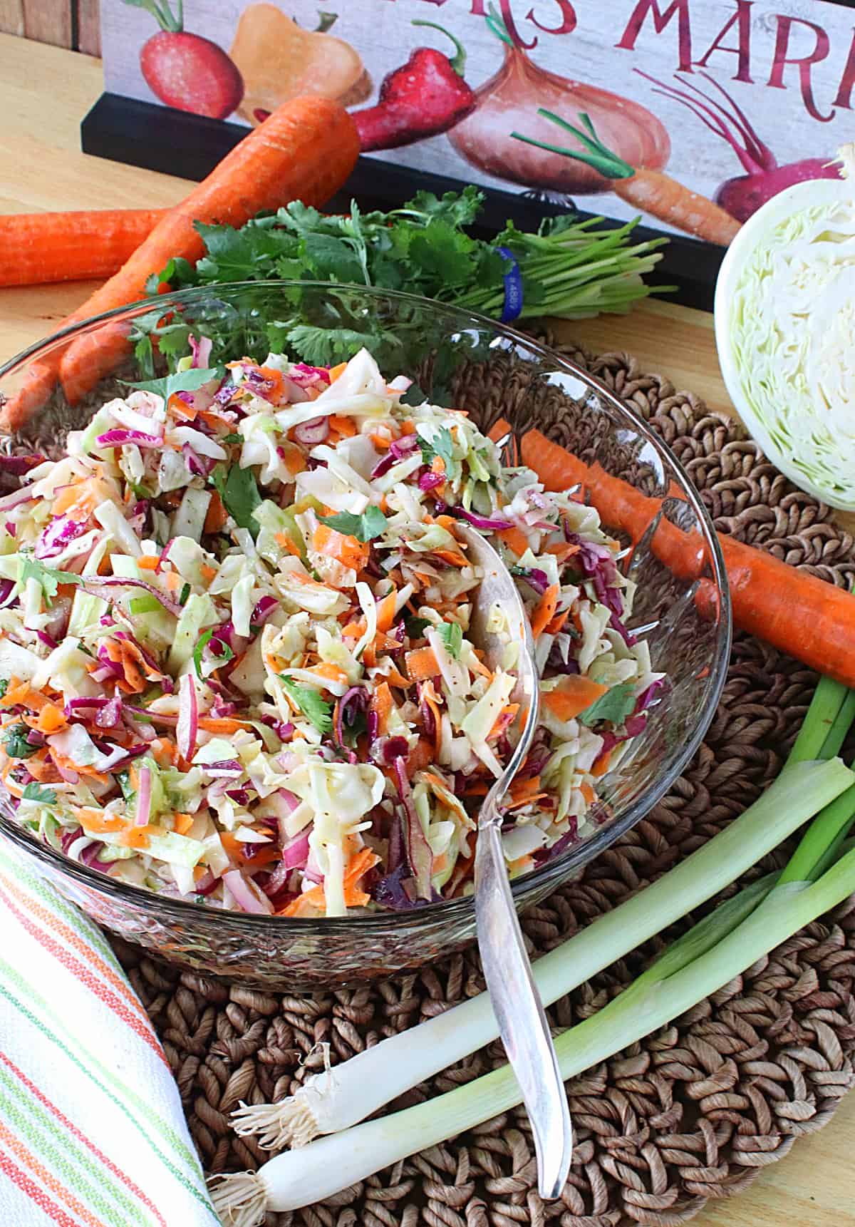 A glass bowl filled with a colorful No Mayo Sweet Sour Coleslaw with cabbage and carrots in the background.