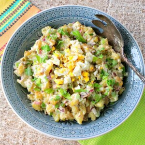 A blue bowl filled with Dijon Potato Salad along with a serving spoon.