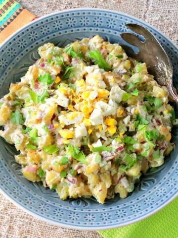 A blue bowl filled with Dijon Potato Salad along with a serving spoon.