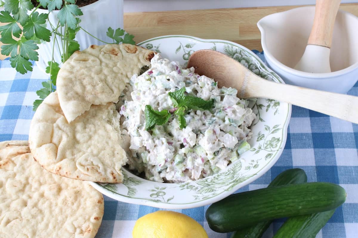 A bowlful of Tzatziki Chicken Salad with a wooden spoon and a pita bread on the side. 