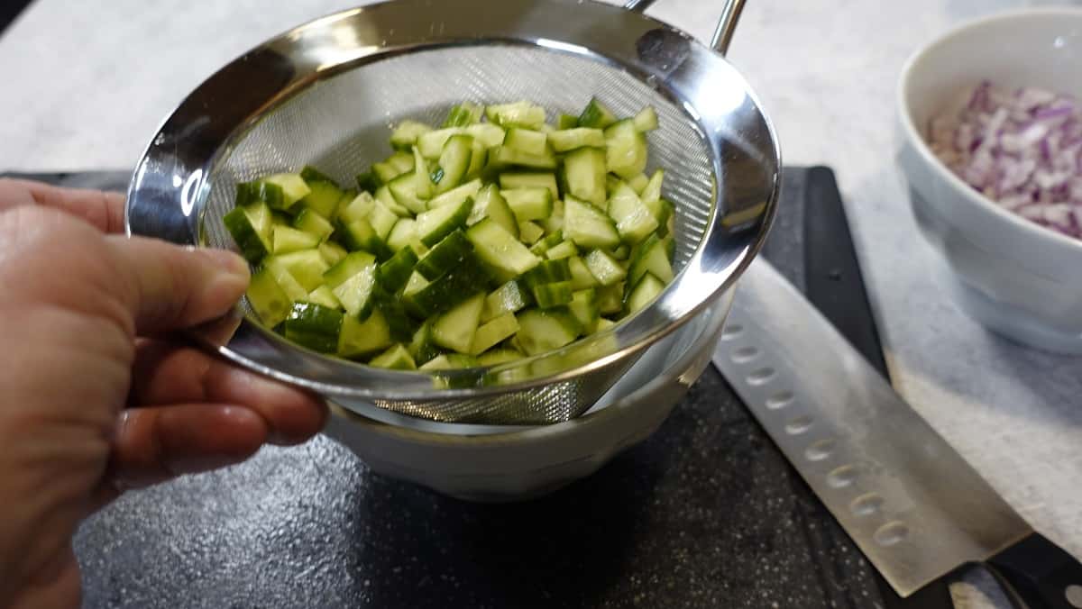 Diced cucumbers in a strainer over to bowl to remove water. 