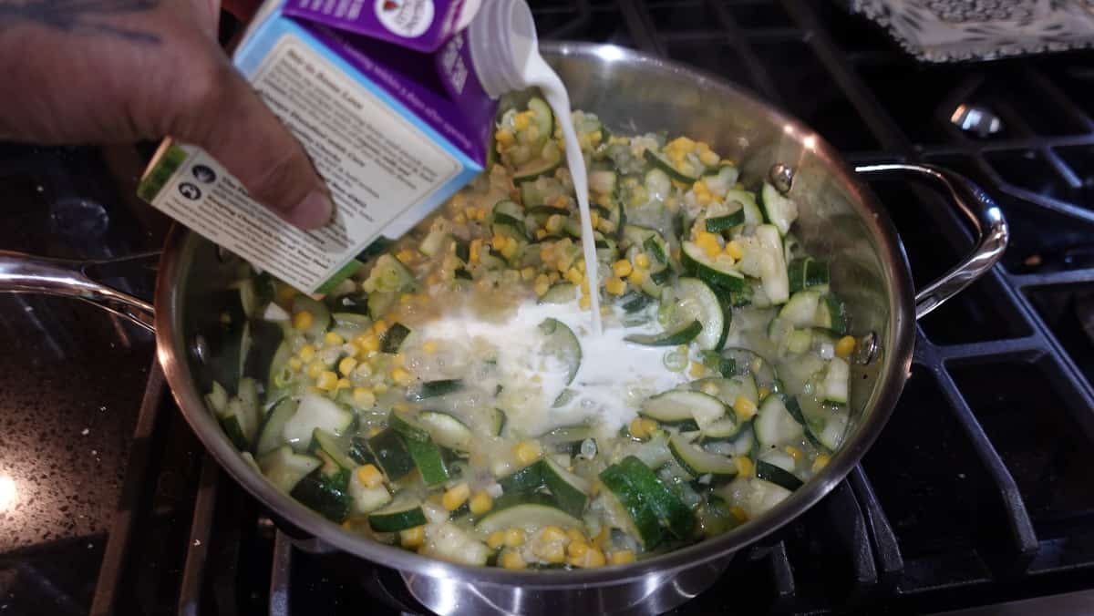 Cream being added to a skillet with zucchini.