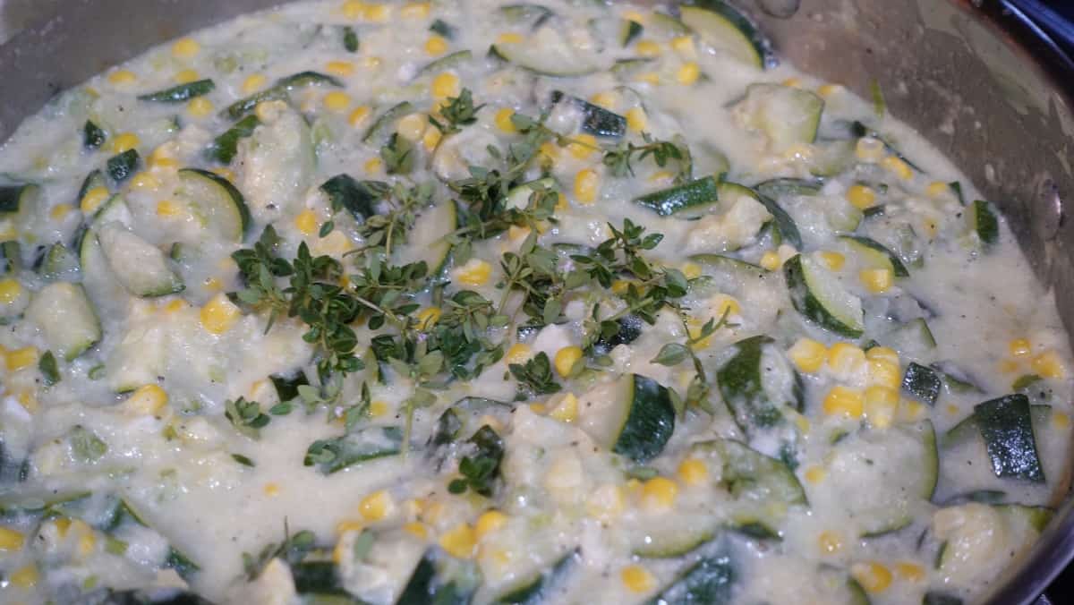 Corn and zucchini gratin in a skillet with thyme.