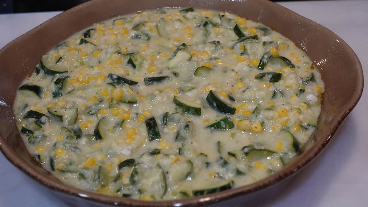 A zucchini and corn gratin in a round tan casserole dish.