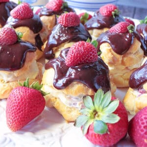 Chocolate Strawberry Cream Puffs on a platter with fresh strawberries on top.