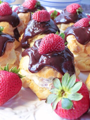 Chocolate Strawberry Cream Puffs on a platter with fresh strawberries on top.