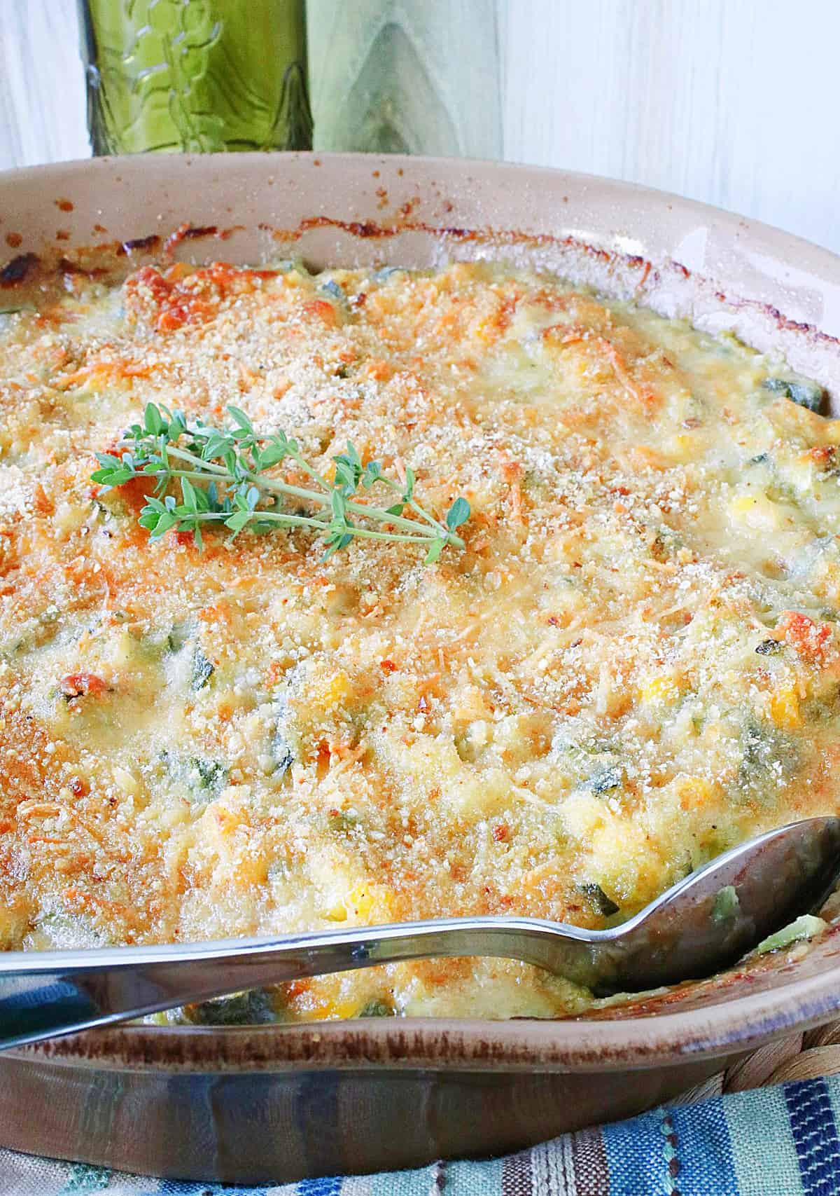 A brown casserole dish filled with baked Zucchini Corn Gratin along with a serving spoon.