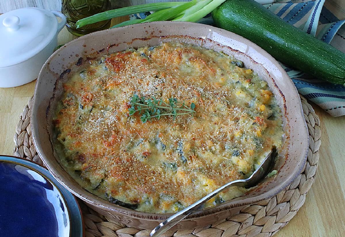 A round tan casserole dish filled with Zucchini Corn Gratin and a spoon. 