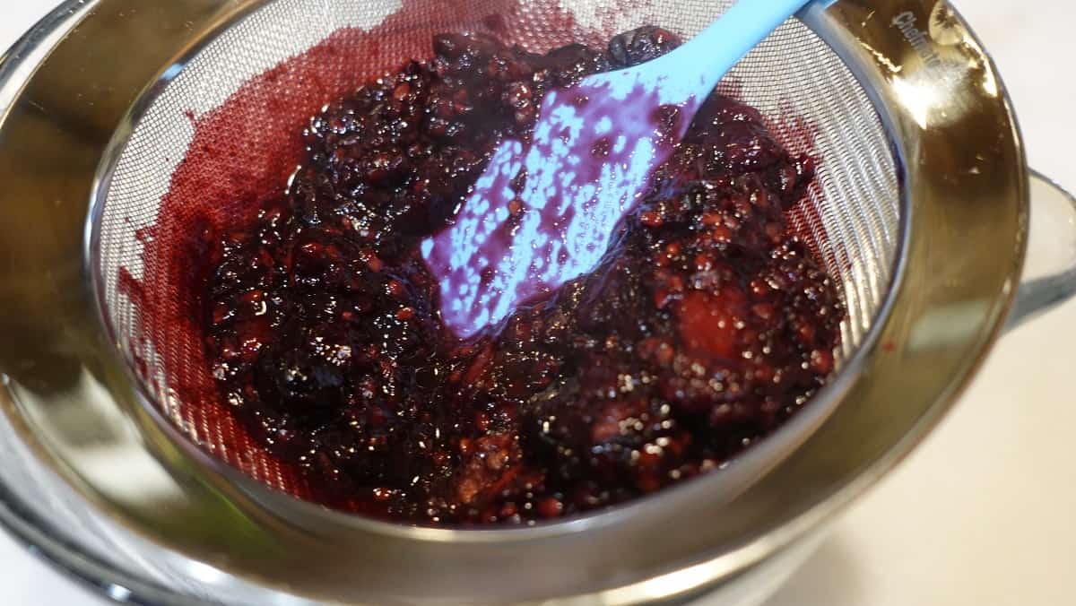 Cooked berries and a spatula in a strainer.