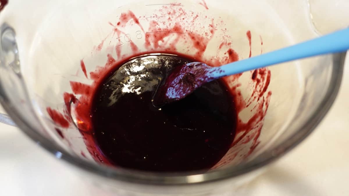 The juice from cooked berries in a bowl with a blue spatula.