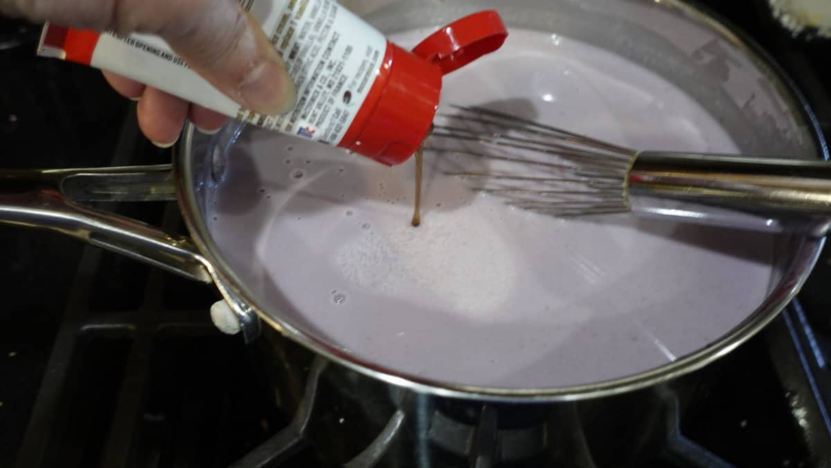 Vanilla paste being added to a gelato base in a saucepan.