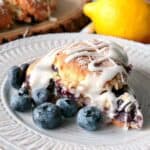A Blueberry Lemon Scone on a white plate with fresh blueberries.