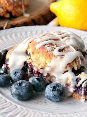 A Blueberry Lemon Scone on a white plate with fresh blueberries.