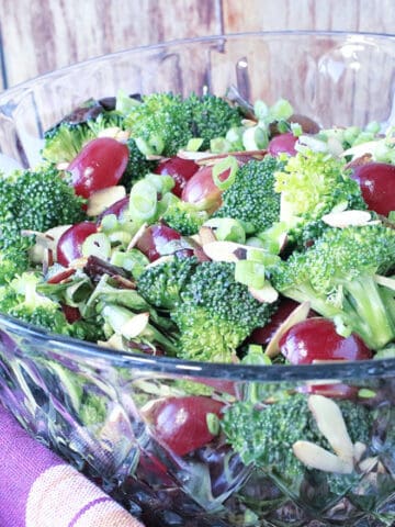 A glass bowl filled with Sweet and Sour Broccoli Salad with fresh broccoli, red grapes, and slivered almonds.