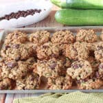 A baking sheet filled with Zucchini Oatmeal Cookies with chocolate covered raisins in the background.