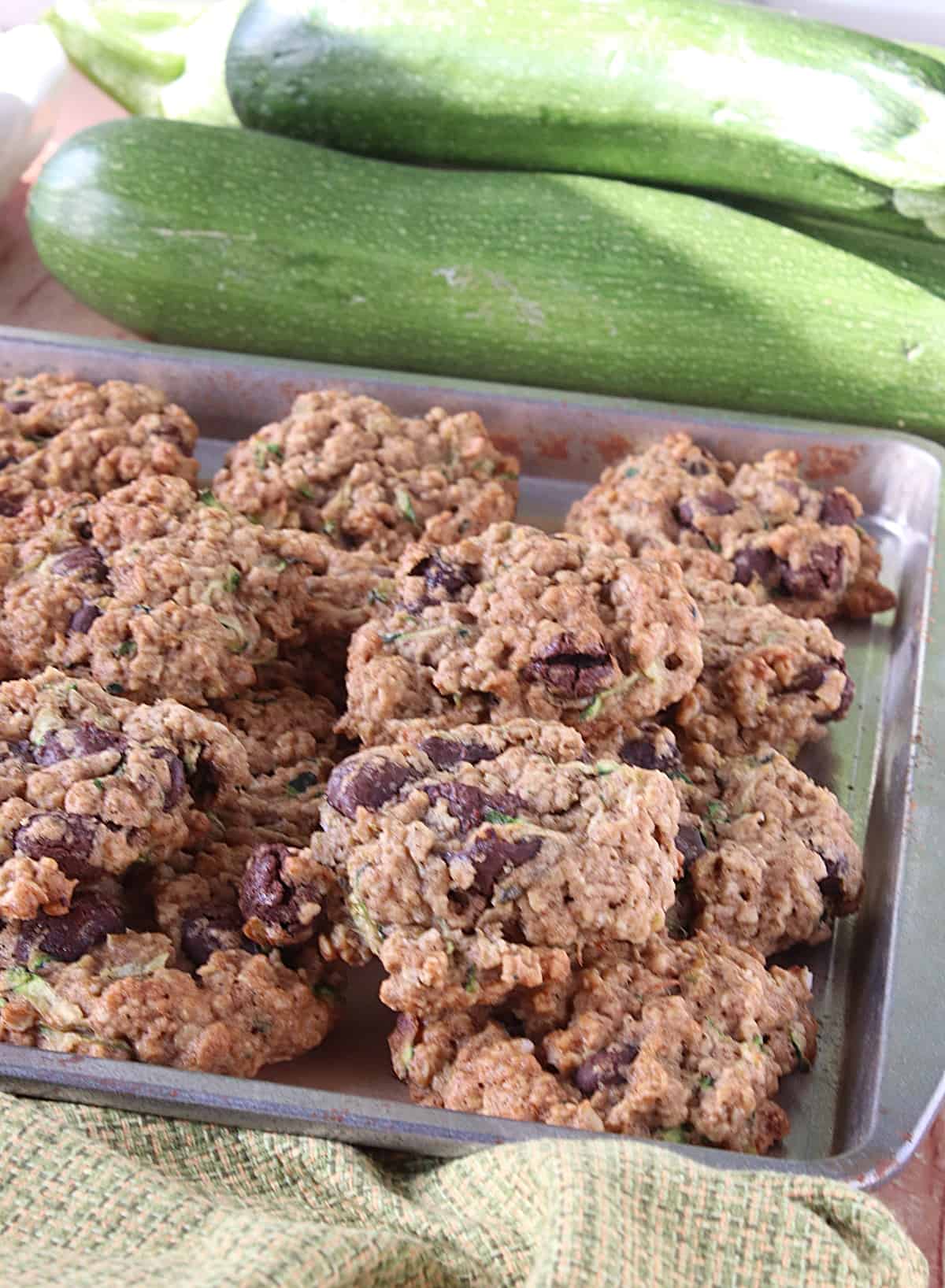 A cookie sheet filled with Zucchini Oatmeal Cookies with whole zucchini in the background.