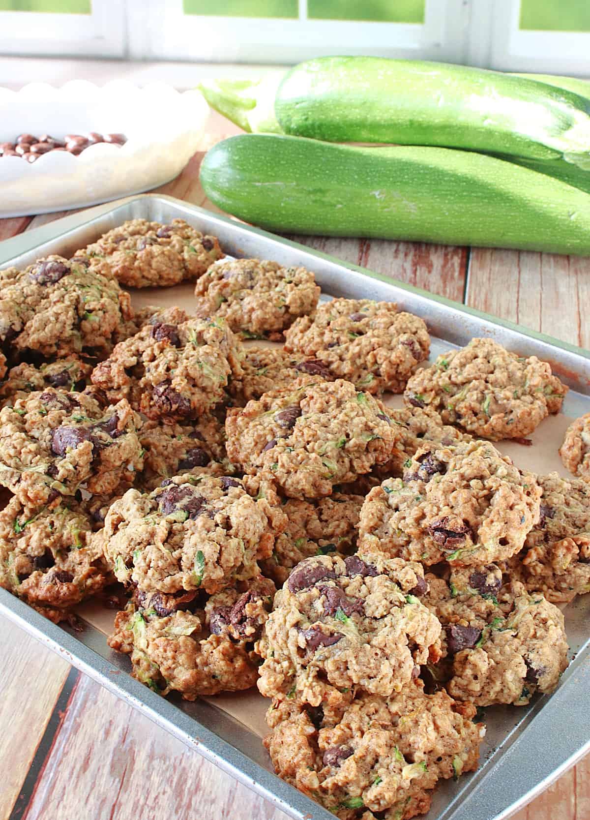 A cookie sheet filled with Zucchini Oatmeal Cookies with zucchini in the background.