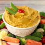 A bowl of Chickpea and Carrot Hummus surrounded by vegetables.