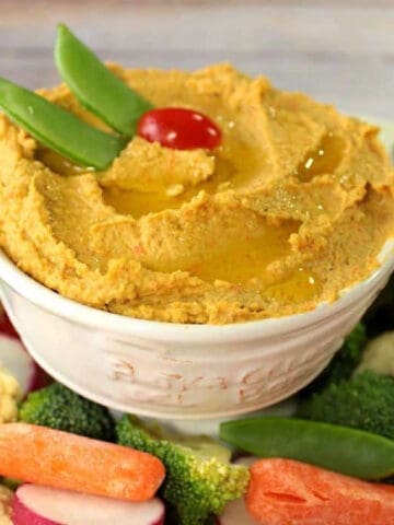 A bowl of Chickpea and Carrot Hummus surrounded by vegetables.