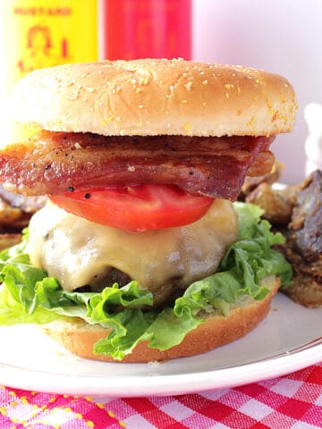 A burger topped with pork belly and tomato.